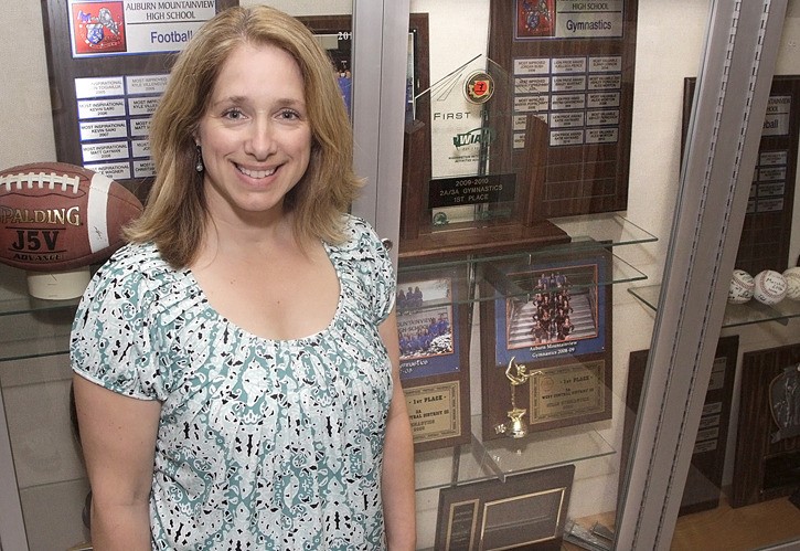 Auburn Mountainview gymnastics coach Jayme Hostetter in front of the high school's trophy case and the first-place gymnastics trophy.