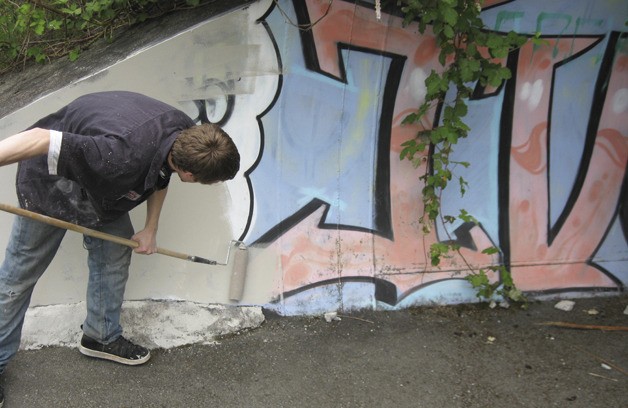 A teen applies a fresh coat of paint over graffiti in south Auburn as part of his restitution.