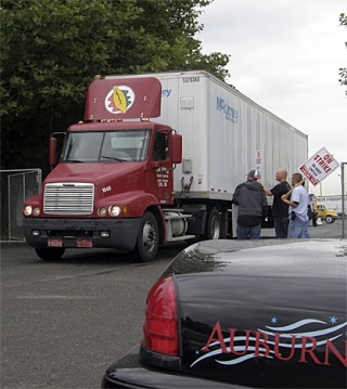 Striking Teamsters look on as a replacement driver exits the Oak Harbor Freight Lines' yard off 37th Street Northwest on Thursday. Police units arrived on the scene to keep the roadway open to truckers.