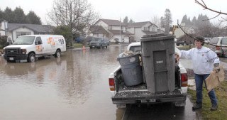 Patty Wingate loads a pickup truck with wet debris Monday from the Pacific home of Chad Weichinger