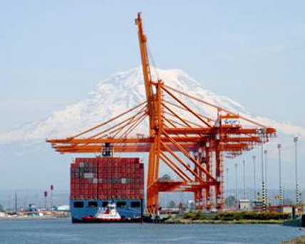 Modern cranes move containers directly from the ship to railcars at the Port of Tacoma with Mount Rainier in the background.