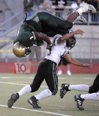 Auburn’s Chris Young goes over Kentwood’s Zach Corpuz for a touchdown in the first quarter of the Trojans’ 28-7 victory over the Conquerors last Friday night.