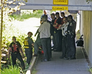 Officers from the Kent and Tukwila Fire departments and Tukwila police huddle underneath the Strander Boulevard bridge on the banks of the Green River after the Kent Fire Boat retrieved the body of a man from the water.