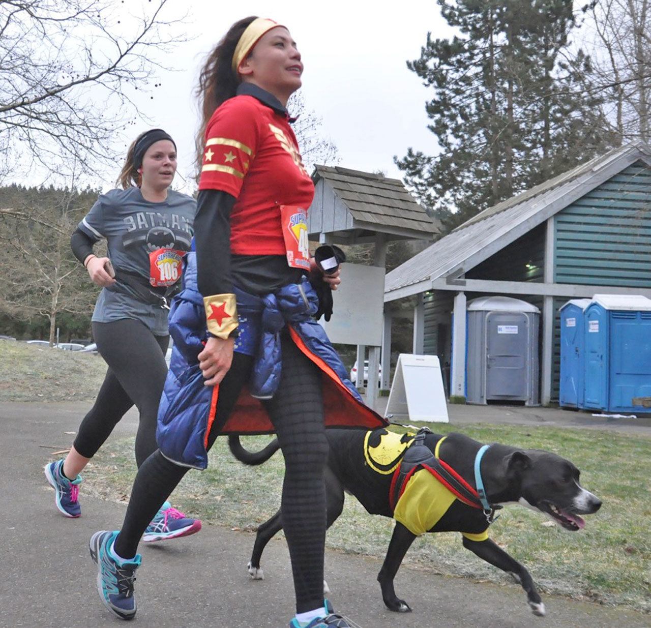Megan Brown runs with her dog, Goose, as Batman, with Evelyn Hernandez.