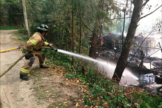 A firefighter douses what’s left of a Wednesday morning fire that destroyed a small vacant home and damaged a travel trailer in Pacific. COURTESY PHOTO, VRFA