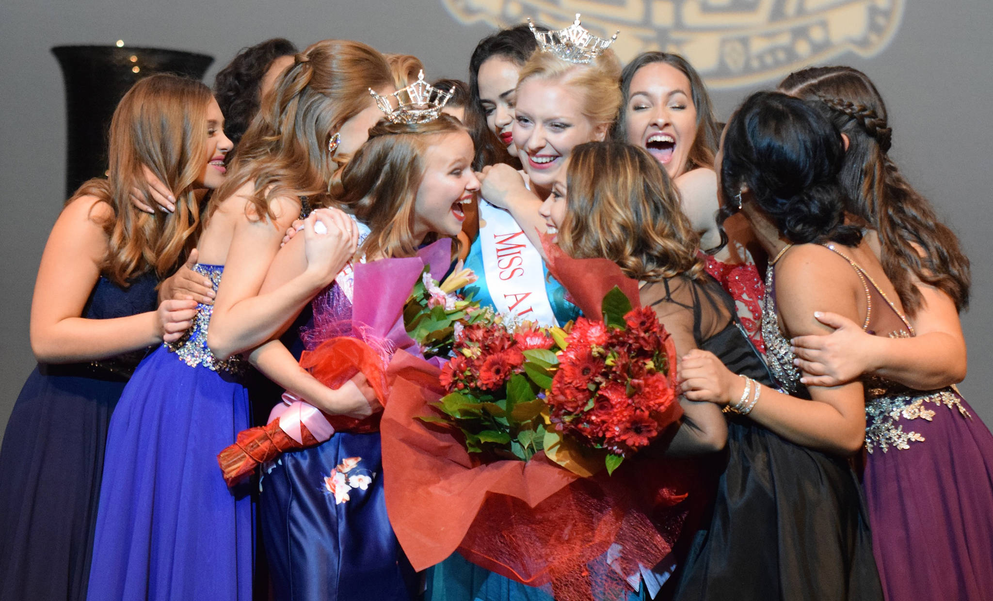 Contestants swarm Whitney Van Vleet, wearing the coveted crown, right, after she won the Miss Auburn title at the Performing Arts Center on Saturday night. Olivia Thomas, with the tiara, left, earlier took Miss Auburns Outstanding Teen title. RACHEL CIAMPI, Auburn Reporter