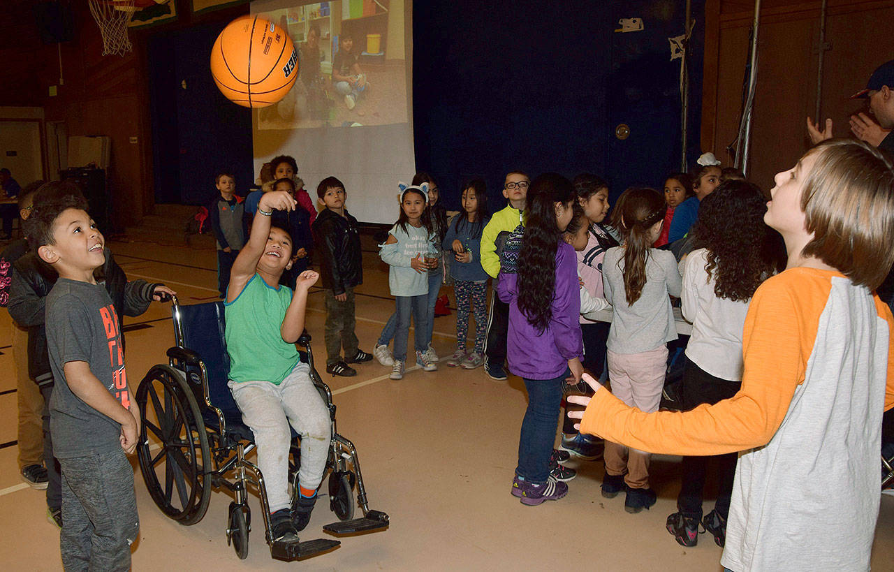 Volunteer Kosta Everson has first-grader CJ Jumawan shoot a basketball in a wheelchair as classmate Malachi Dorsey watches during Disability Awareness Day at Evergreen Heights Elementary School. RACHEL CIAMPI, Auburn Reporter