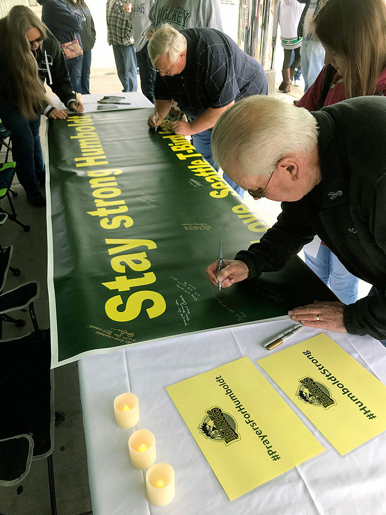 Bruce McDonald, foreground, and his 15-year-old granddaughter, Chloe, join others outside the accesso ShoWare Center on Saturday in signing a banner supporting the Humboldt, Saskatchewan junior hockey team. MARK KLAAS, Kent Reporter
