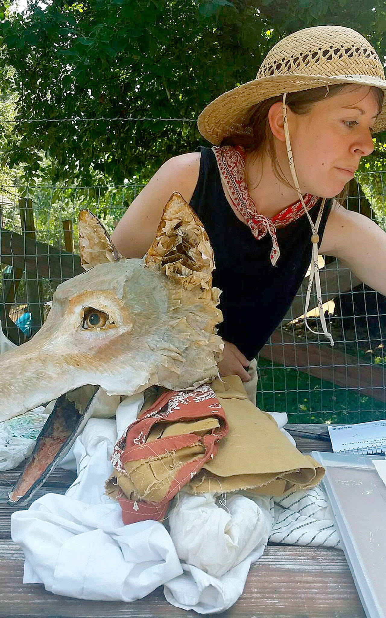 Michelle Lassaline, Mary Olson Farm’s artist in residence, and Coyote, one of 11 paper-maché masks she has made and dons when she paints for the public, enjoy a cool moment in the welcome shade of an apple tree on her final day at the rebuilt farm last Sunday. ROBERT WHALE, Auburn Reporter