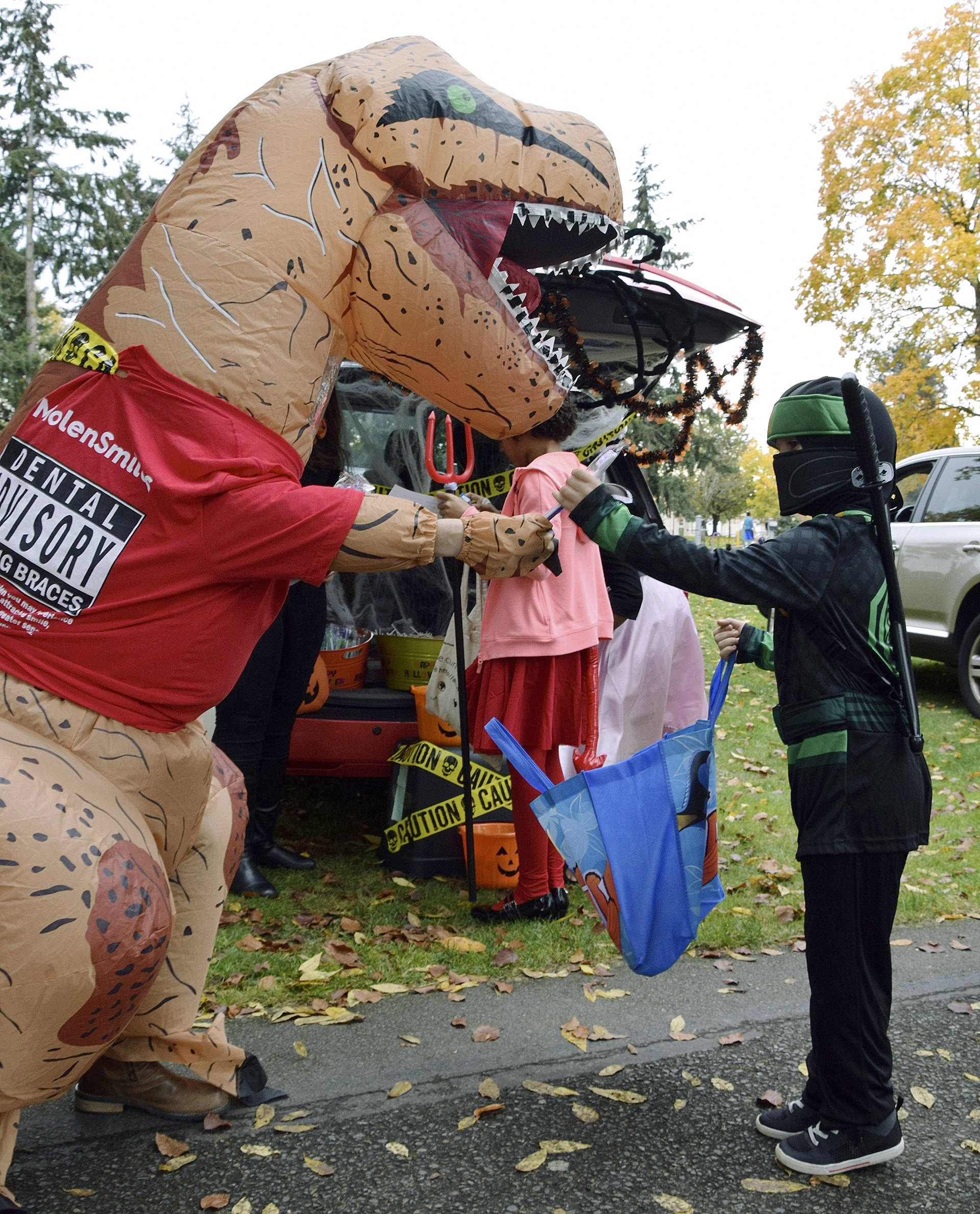 Left, Sebastian Bane, 5, gets a toothbrush from T-Rex. Right, Krystal Sanders as a pirate has Shaylee Bonzan, 9, and Landon Gregory, 7, pluck candy from the treasure chest.
