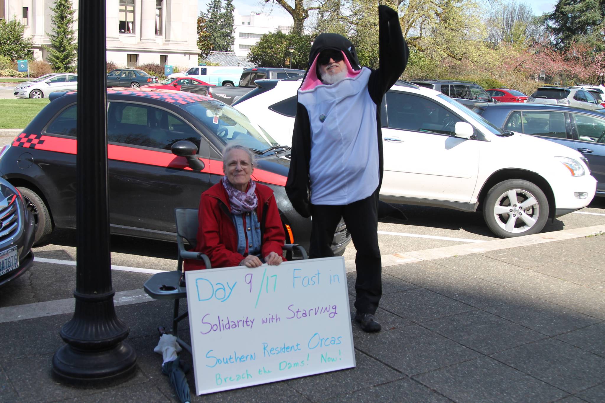 Lanni Johnson sitting in front of the Capitol building steps where she has been on a hunger strike for the last nine days to save the Southern Resident Orcas. Johnson is joined by supporter, Phil Myers, who can be seen in an orca onesie. COURTESY PHOTO, Emma Epperly, WNPA Olympia News Bureau