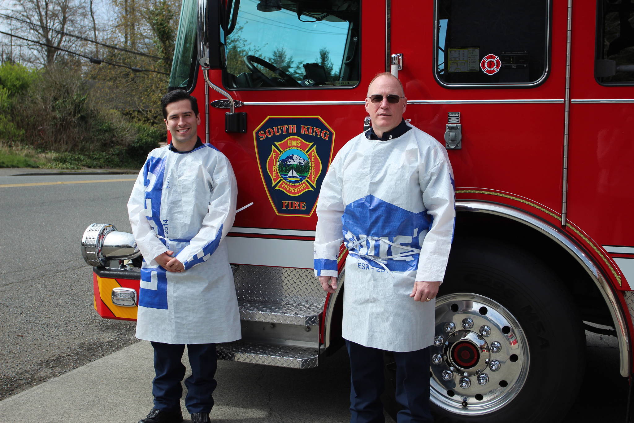Firefighter Brett Connelly, left, and Driver Engineer Jim Wilson wear the handmade protective gowns, sewn by Wilson with materials donated from Lowe’s Home Improvement store in Federal Way. Olivia Sullivan/staff photo