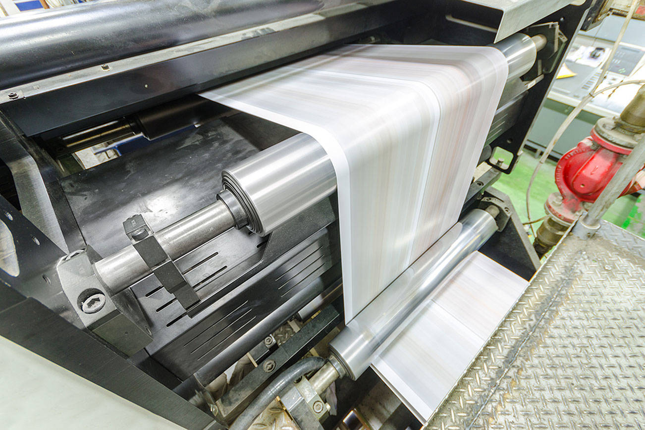 A large webset offset printing press running a long roll off paper over its rollers at high speed. File photo