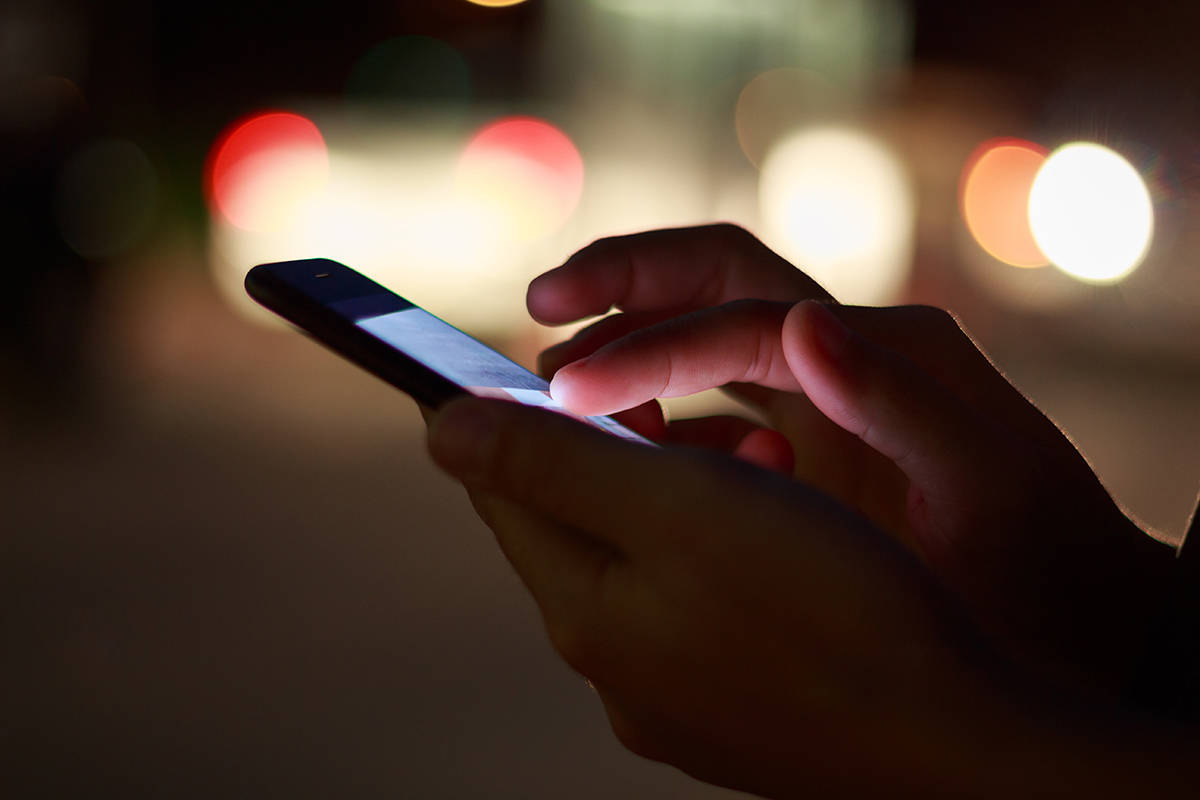 Close-up hand using phone in night time on street. File photo