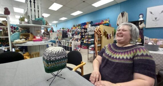 Jen Reeves, wearing a sweater she has woven, throws herself back in a chair to indulge in one of her favorite activities, laughter, at her yarn shop Little Knittym at the corner of East Main and Auburn Avenue. Photo by Robert Whale, Auburn Reporter.