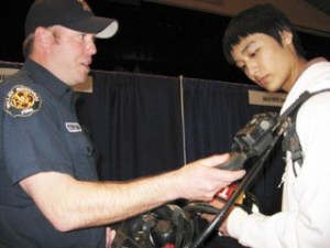 Firefighter Dean McAuley of the Valley Regional Fire Authority explains  some of the gear he uses to Thom Phan