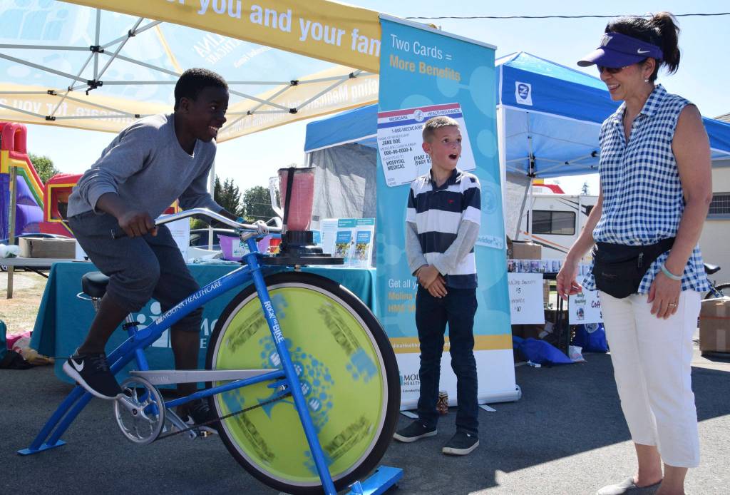 Carrie Ching from Molina Healthcare has Trocen Cooper, 12, ride a stationary bike that makes a smoothie drink as Tristyn Crockett, 9, watches.