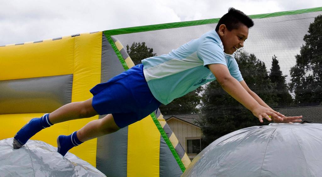 Brian Silva, above, jumps on the inflatable in Les Gove Park at the AuburnFest. Right, Joycelyn, 10, and Lupe Gutierrez, 7, sail down the slide in the rain at the park.