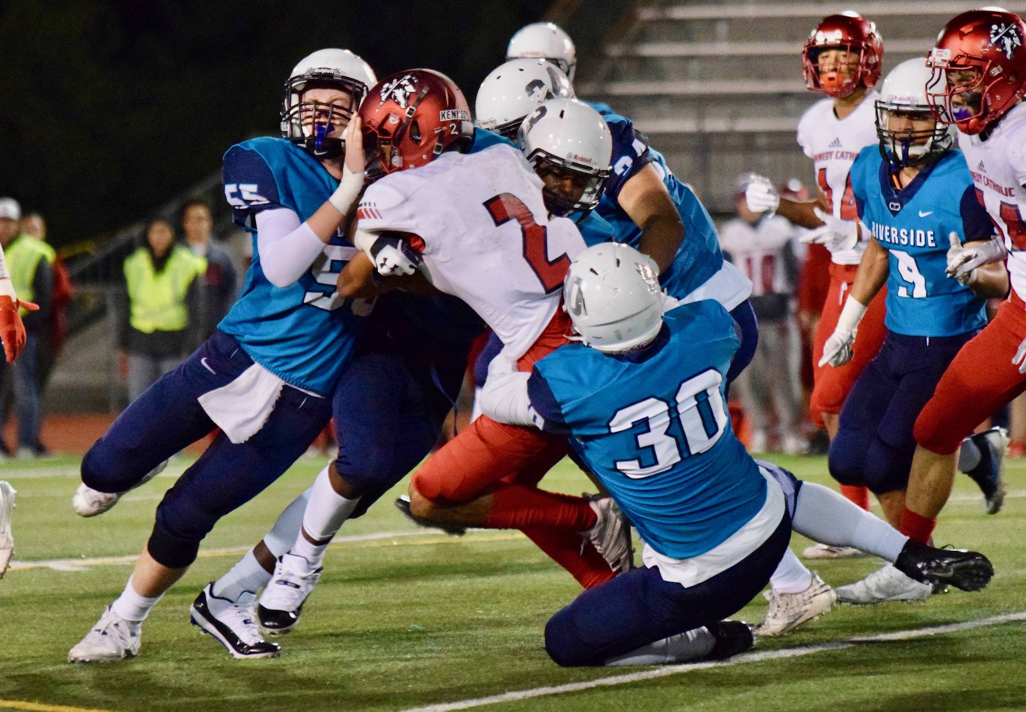 Auburn Riverside defenders Cade Foster (55), Sam Spicciati (30) and Jarrece Garner (3) converge to bring down Kennedy Catholics Junior Alexander during North Puget Sound League Mountain Division action last Friday night at Auburn Memorial Stadium. RACHEL CIAMPI, Auburn Reporter