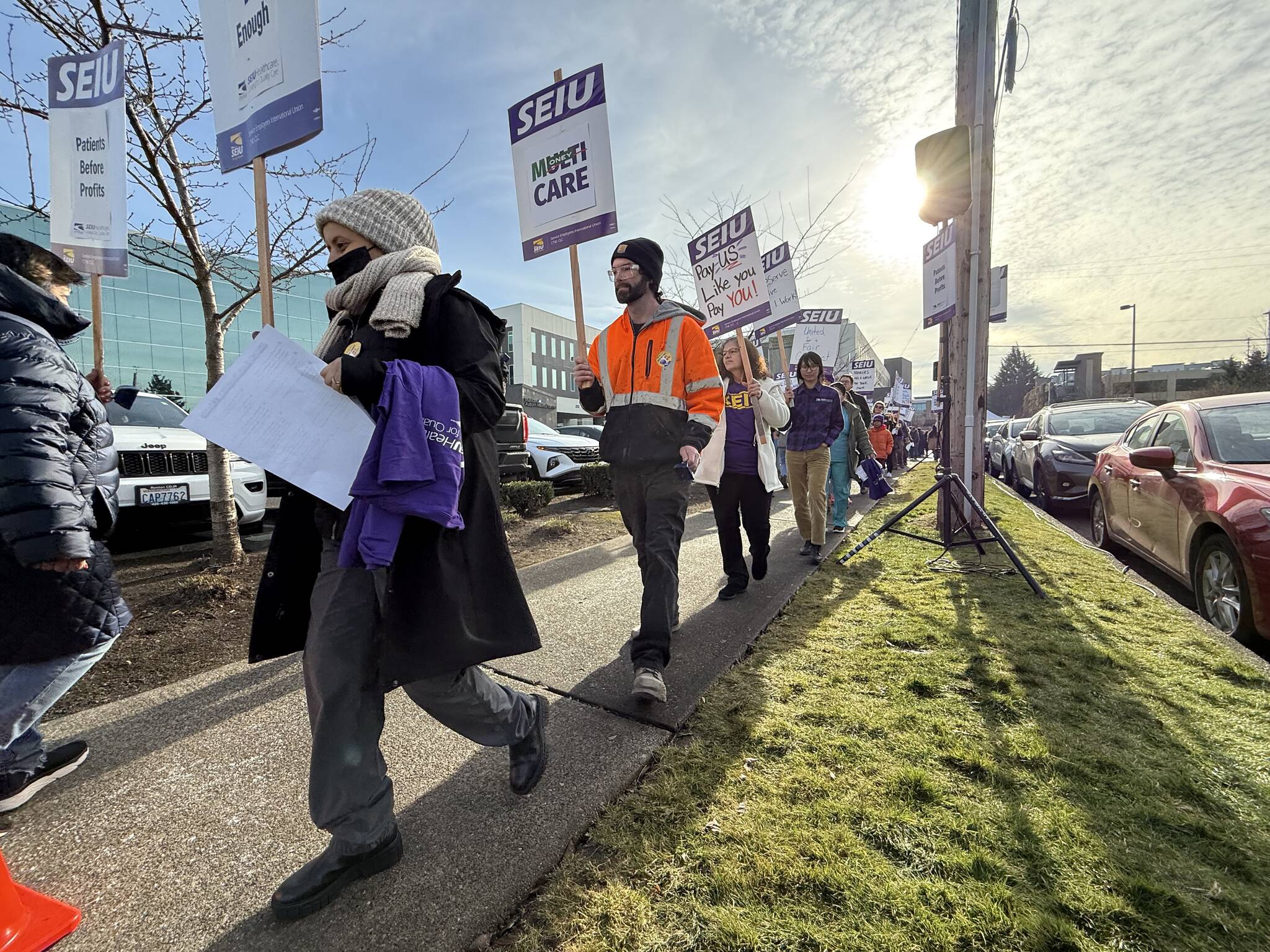 Marchers protesting for better wages on the sidewalk along the hospital front.